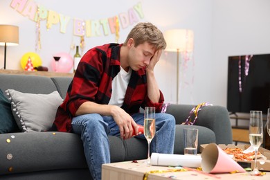 Photo of Man suffering from hangover on sofa in messy room after party