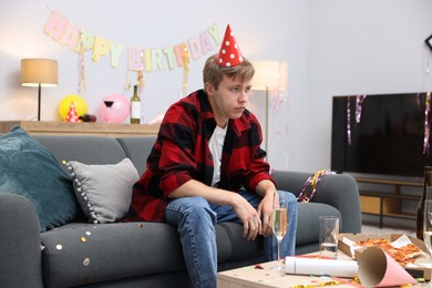Photo of Man suffering from hangover on sofa in messy room after party
