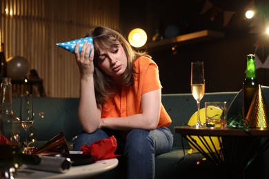 Photo of Woman suffering from hangover on sofa in messy room after party