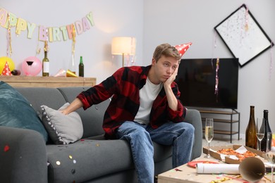 Photo of Man suffering from hangover on sofa in messy room after party