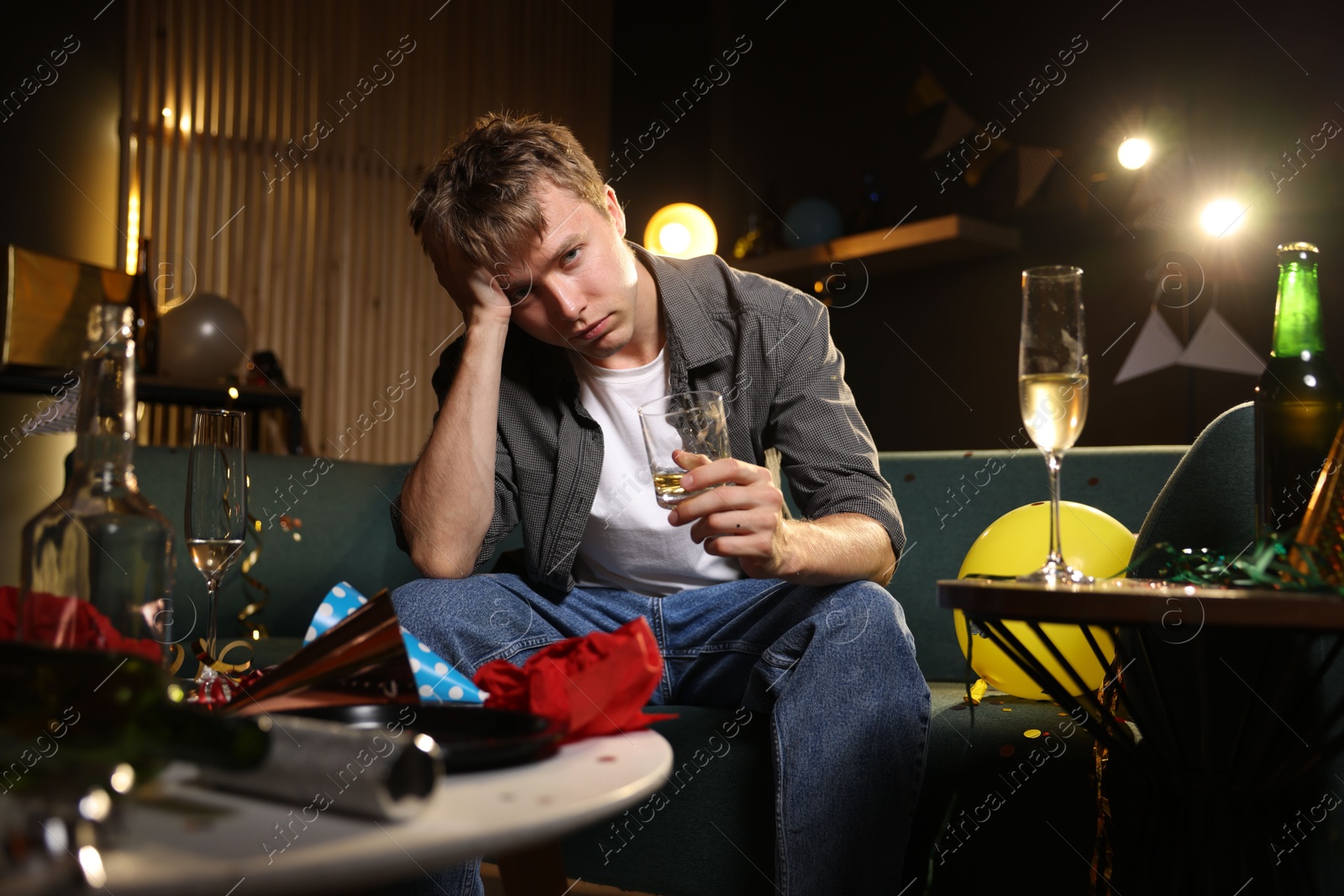 Man with glass of alcohol suffering from hangover on sofa in messy room after party Photo of Man with glass of alcohol suffering from hangover on sofa in messy room after party