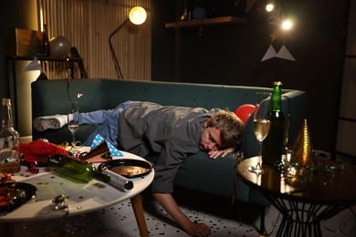 Photo of Man suffering from hangover on sofa in messy room after party