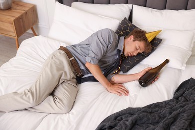 Photo of Man with alcohol suffering from hangover on bed indoors, above view