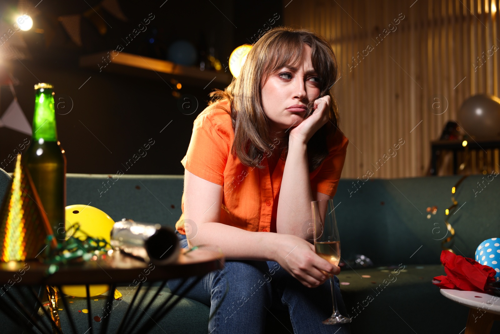 Photo of Woman with glass of alcohol suffering from hangover on sofa in messy room after party