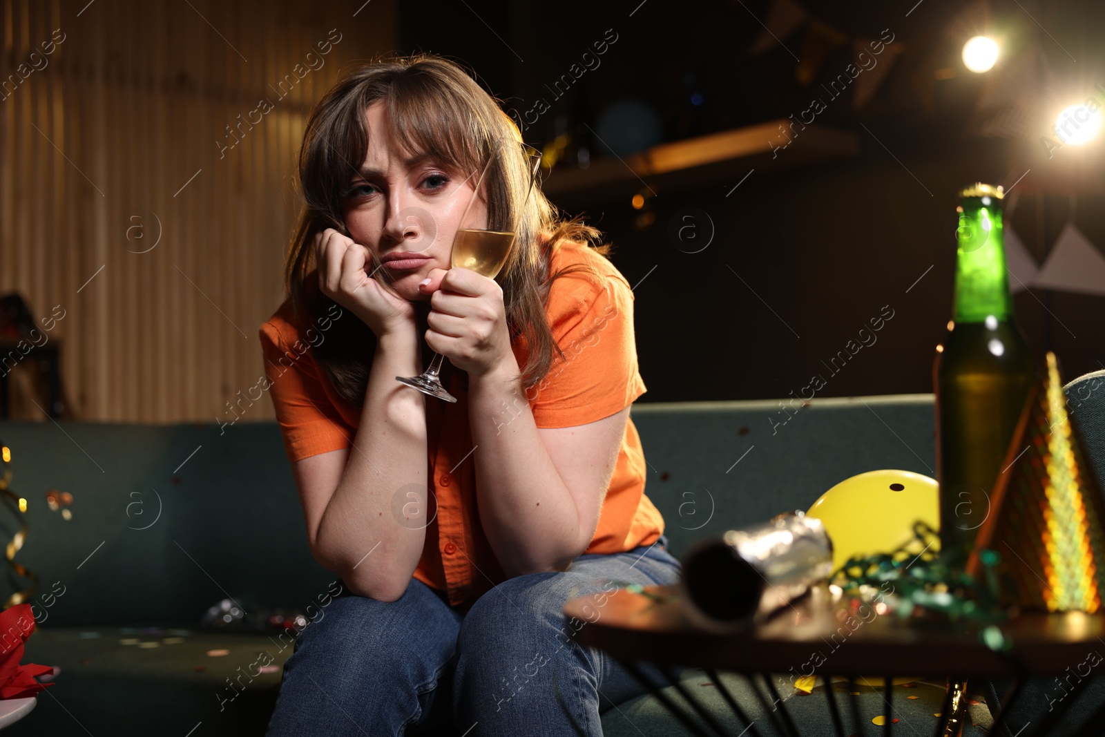 Photo of Woman with glass of alcohol suffering from hangover on sofa in messy room after party