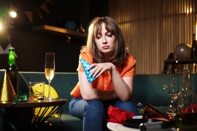 Photo of Woman suffering from hangover on sofa in messy room after party