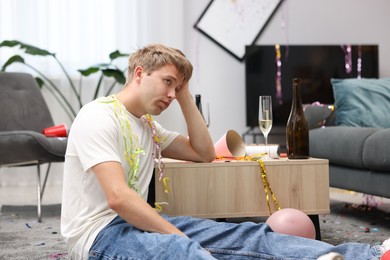 Photo of Man suffering from hangover on floor in messy room after party
