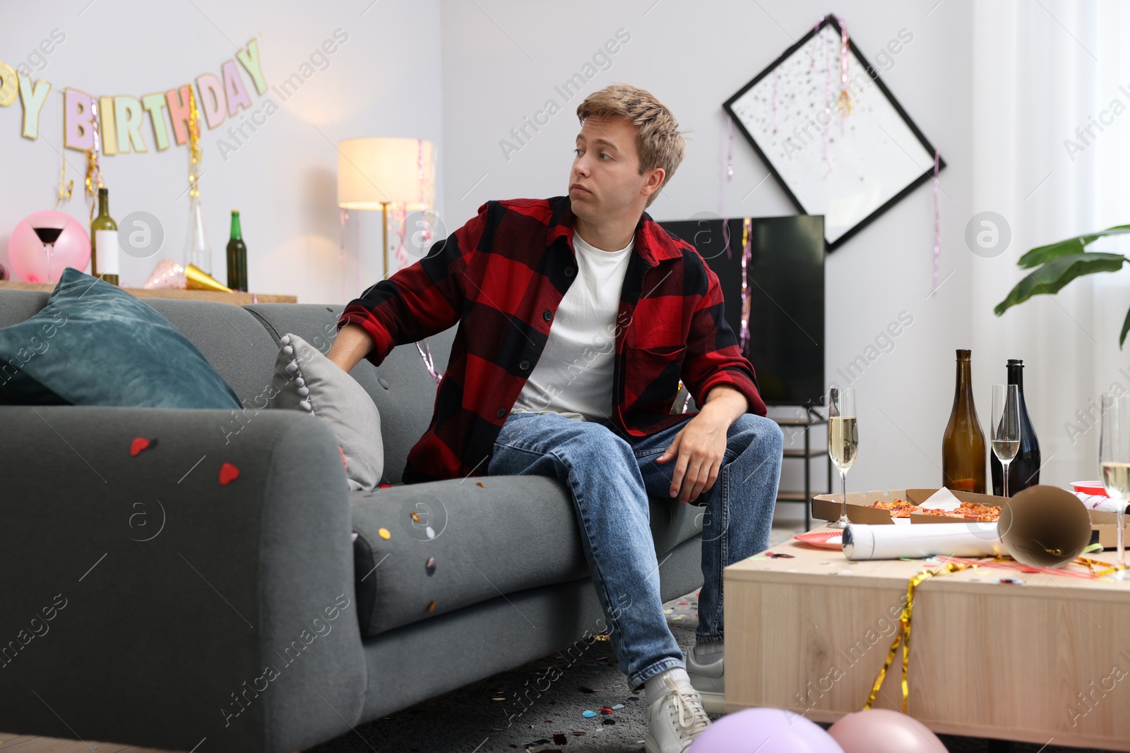 Man suffering from hangover on sofa in messy room after party Photo of Man suffering from hangover on sofa in messy room after party