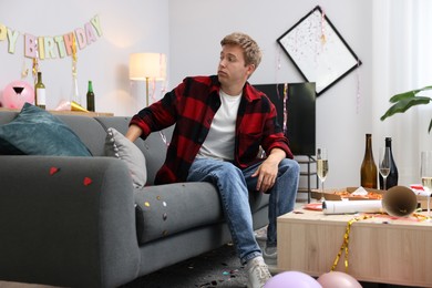 Photo of Man suffering from hangover on sofa in messy room after party