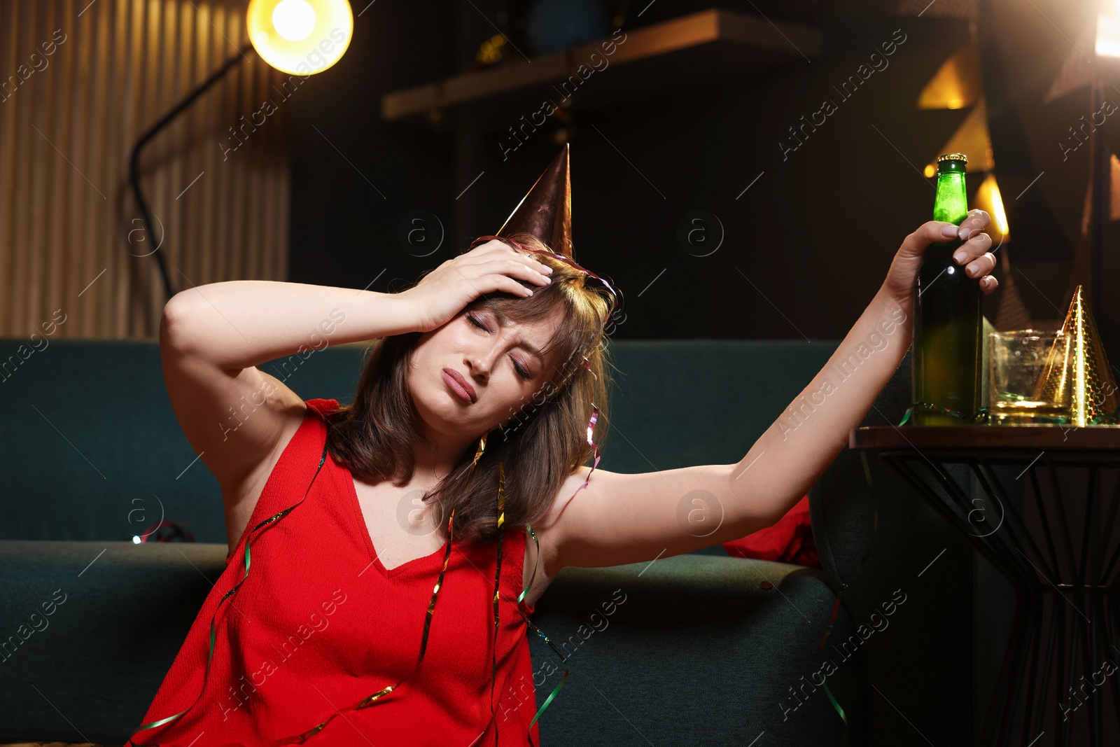 Woman with bottle of beer suffering from hangover in messy room after party Photo of Woman with bottle of beer suffering from hangover in messy room after party