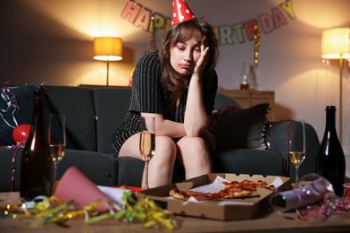 Photo of Woman suffering from hangover on sofa in messy room after party