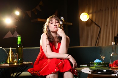 Photo of Woman with glass of alcohol suffering from hangover on sofa in messy room after party