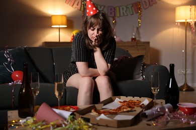 Photo of Woman suffering from hangover on sofa in messy room after party
