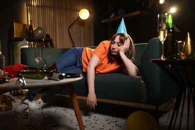 Photo of Woman suffering from hangover on sofa in messy room after party