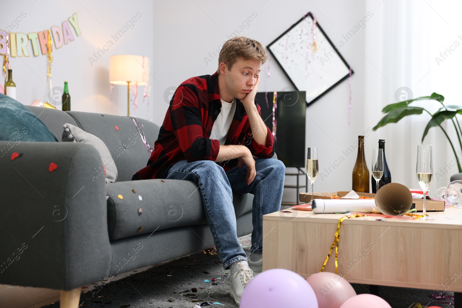 Man suffering from hangover on sofa in messy room after party Photo of Man suffering from hangover on sofa in messy room after party