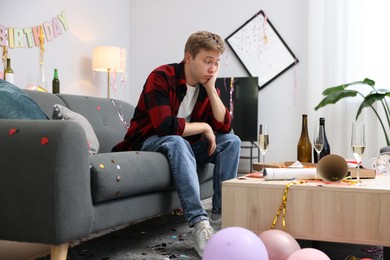Photo of Man suffering from hangover on sofa in messy room after party