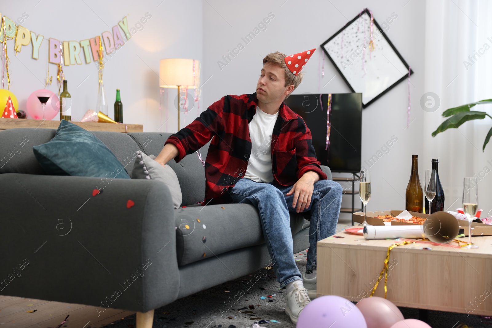 Man suffering from hangover on sofa in messy room after party Photo of Man suffering from hangover on sofa in messy room after party