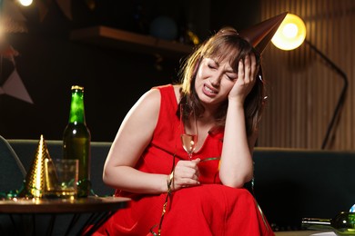 Photo of Woman with glass of alcohol suffering from hangover on sofa in messy room after party