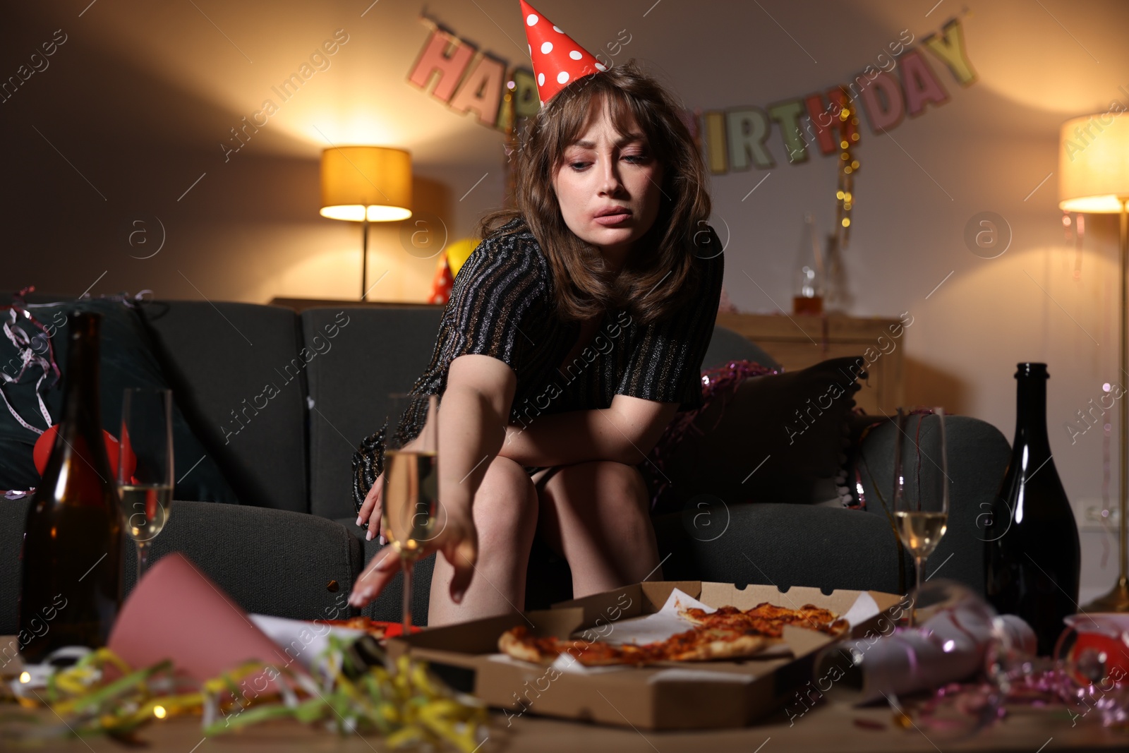 Woman taking glass of alcohol and suffering from hangover in messy room after party Photo of Woman taking glass of alcohol and suffering from hangover in messy room after party