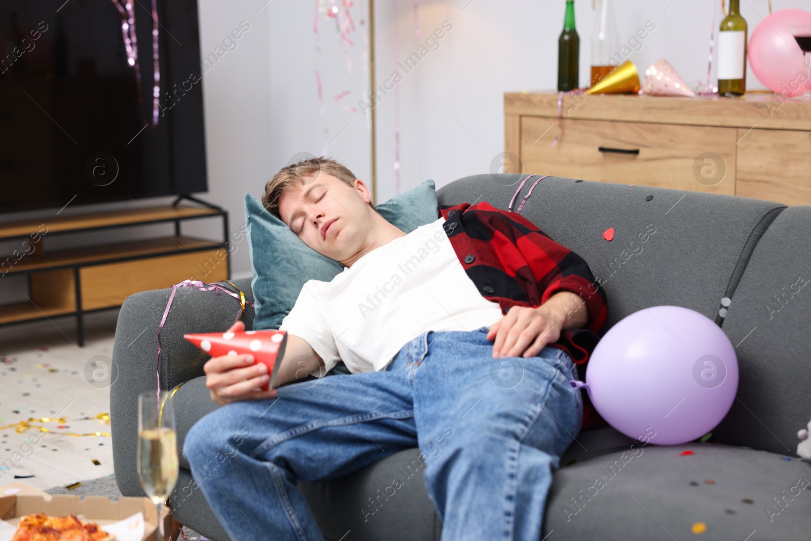 Man suffering from hangover on sofa in messy room after party Photo of Man suffering from hangover on sofa in messy room after party