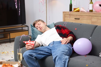 Photo of Man suffering from hangover on sofa in messy room after party