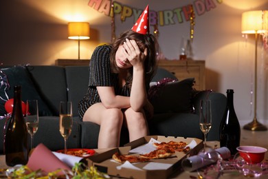 Photo of Woman suffering from hangover on sofa in messy room after party