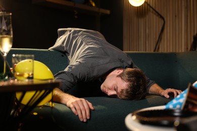 Photo of Man suffering from hangover on sofa in messy room after party