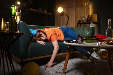 Photo of Woman suffering from hangover on sofa in messy room after party