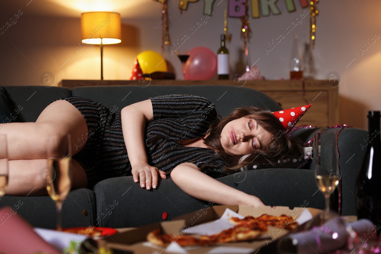 Photo of Woman suffering from hangover on sofa in messy room after party