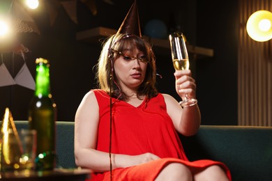 Photo of Woman with glass of alcohol suffering from hangover on sofa in messy room after party