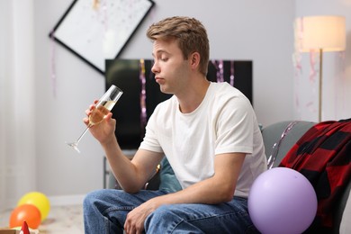 Photo of Man with glass of alcohol suffering from hangover on sofa in messy room after party