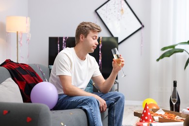 Photo of Man with glass of alcohol suffering from hangover on sofa in messy room after party