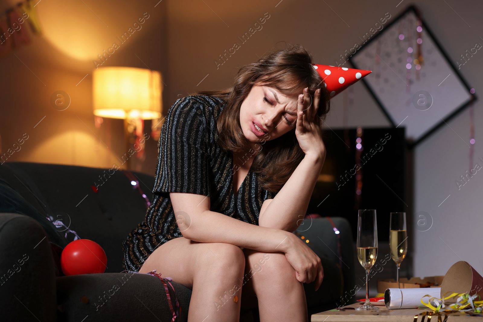 Photo of Woman suffering from hangover on sofa in messy room after party