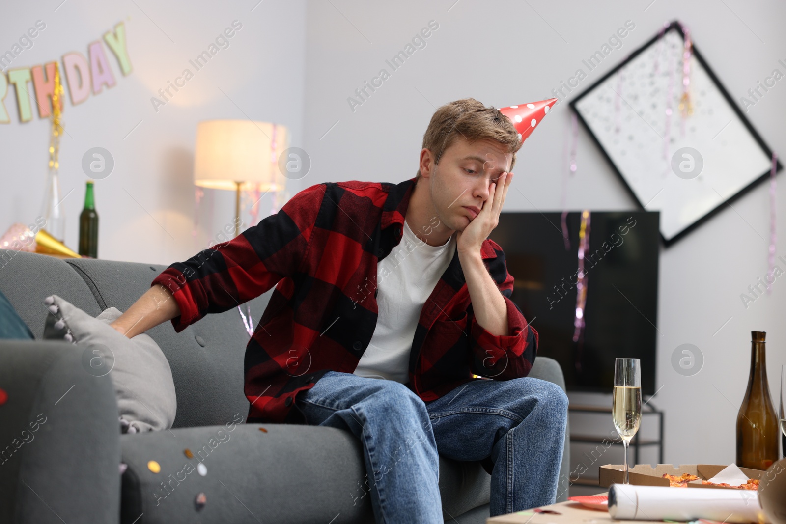 Man suffering from hangover on sofa in messy room after party Photo of Man suffering from hangover on sofa in messy room after party