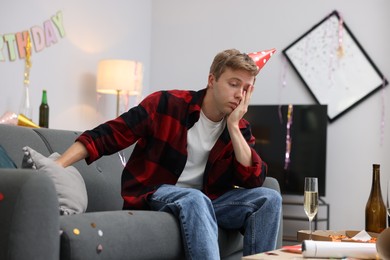 Photo of Man suffering from hangover on sofa in messy room after party