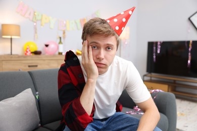 Photo of Man suffering from hangover on sofa in messy room after party