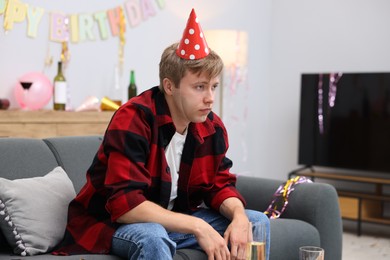 Photo of Man suffering from hangover on sofa in messy room after party
