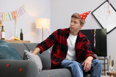 Photo of Man suffering from hangover on sofa in messy room after party