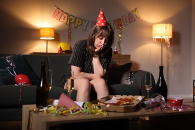 Photo of Woman suffering from hangover on sofa in messy room after party