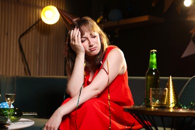 Photo of Woman suffering from hangover on sofa in messy room after party