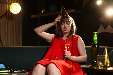 Photo of Woman with glass of alcohol suffering from hangover on sofa in messy room after party