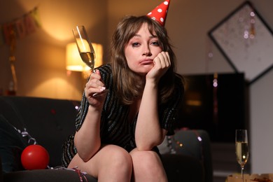 Photo of Woman with glass of alcohol suffering from hangover on sofa in messy room after party