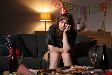 Photo of Woman suffering from hangover on sofa in messy room after party