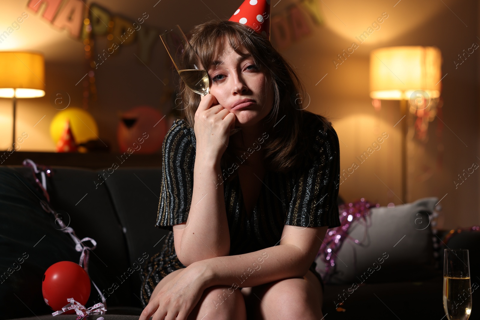 Photo of Woman with glass of alcohol suffering from hangover on sofa in messy room after party
