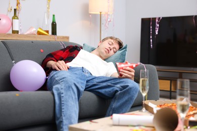 Photo of Man suffering from hangover on sofa in messy room after party