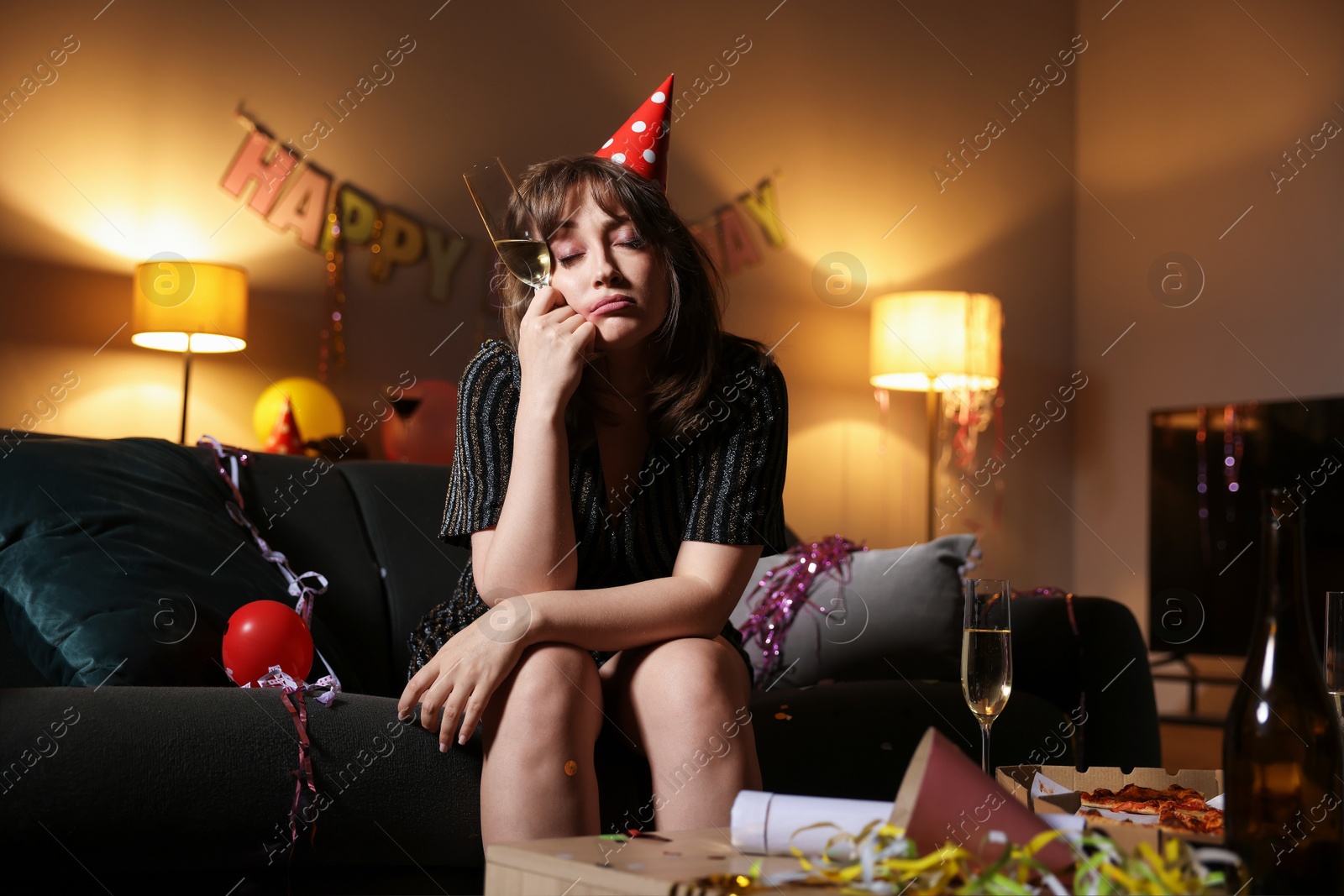 Woman with glass of alcohol suffering from hangover on sofa in messy room after party Photo of Woman with glass of alcohol suffering from hangover on sofa in messy room after party
