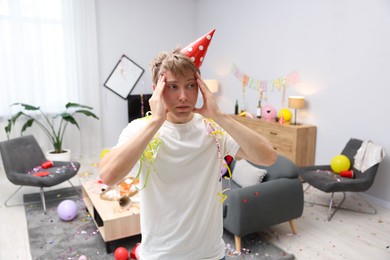 Photo of Man suffering from hangover in messy room after party