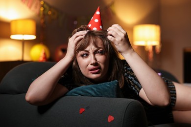 Photo of Woman suffering from hangover on sofa in messy room after party