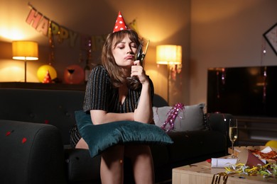 Photo of Woman with glass of alcohol and pillow suffering from hangover on sofa in messy room after party