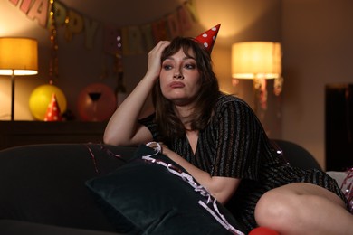 Photo of Woman suffering from hangover on sofa in messy room after party